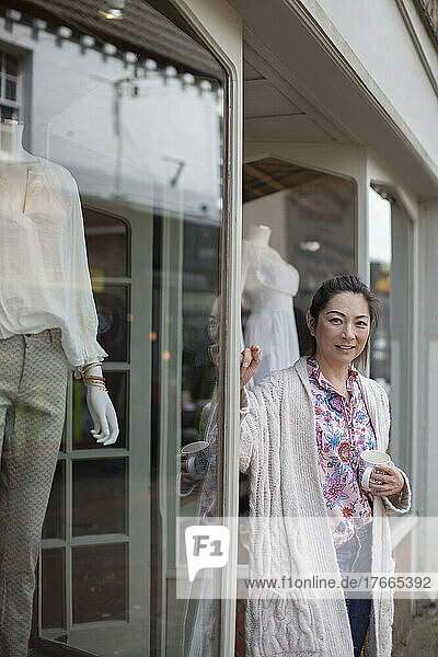 Porträt einer selbstbewussten Geschäftsinhaberin  die vor einer Boutique Kaffee trinkt