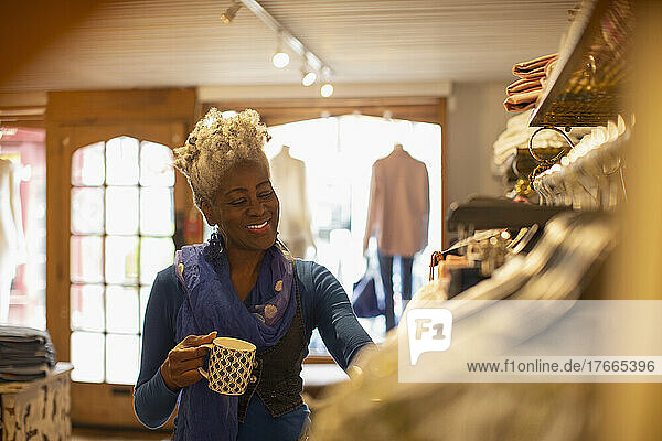 Smiling female shop owner drinking tea in clothing boutique