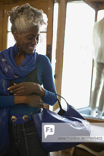 Lächelnde Frau  die eine blaue Handtasche in einer Boutique anprobiert