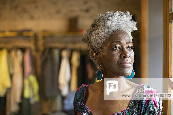 Porträt einer nachdenklichen älteren Ladenbesitzerin  die aus dem Fenster schaut