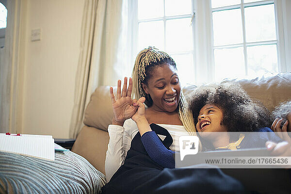 Mother and daughter with digital tablet on living room sofa