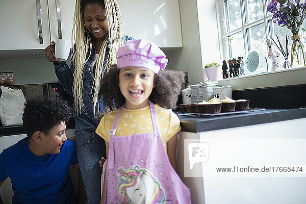 Portrait glückliches Mädchen in Einhornschürze in Küche mit Familie