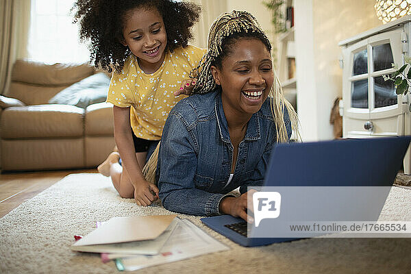 Glückliche Tochter beobachtet Mutter bei der Arbeit am Laptop auf dem Wohnzimmerboden