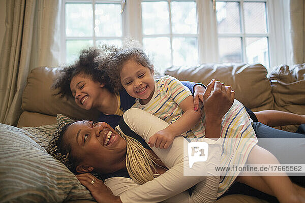 Happy playful mother and daughters on living room sofa