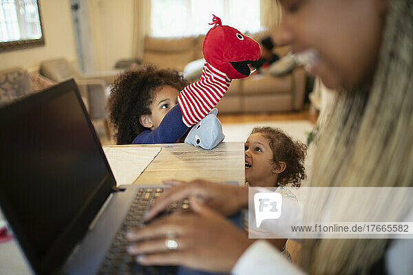 Daughters playing with puppets behind mother working at laptop