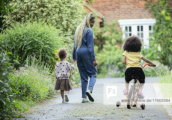 Mother and daughters walking and riding bicycle in driveway