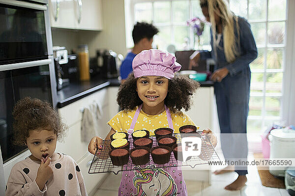 Portrait cute girl holding rack of baked cupcakes in kitchen