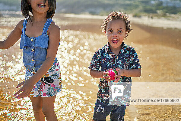 Portrait happy boy with Down Syndrome holding ball on beach