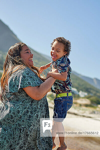 Happy mother lifting cute son with Down Syndrome on beach