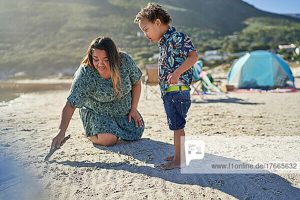 Mother and son with Down Syndrome drawing with stick in sand on beach