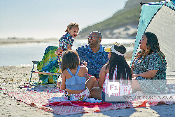 Happy family siting on blanket on sunny summer beach