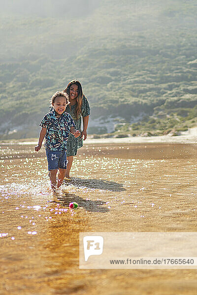 Happy mother and son playing with ball in ocean surf