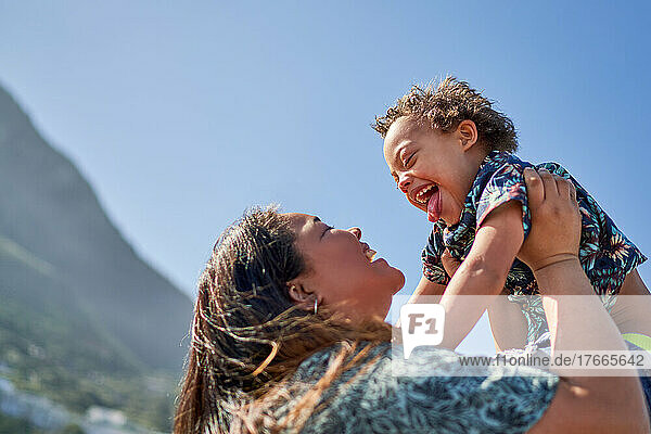 Happy mother lifting son with Down Syndrome below sunny blue sky