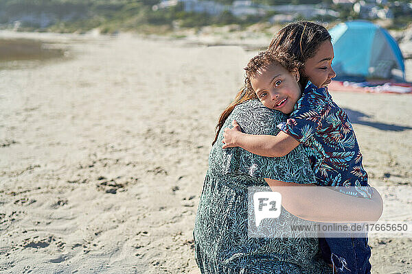 Portrait happy boy with Down Syndrome hugging mother on beach