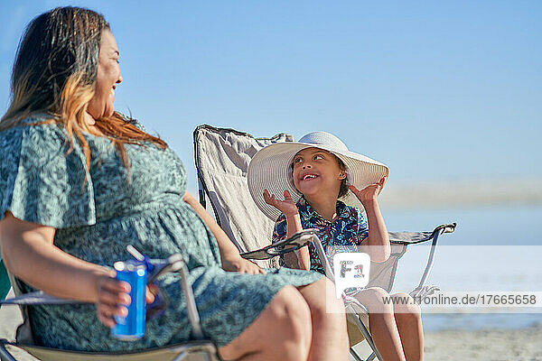 Mother watching happy cute son with Down Syndrome in hat on beach