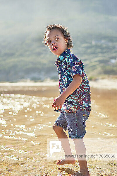 Portrait boy with Down Syndrome wading in ocean on sunny beach