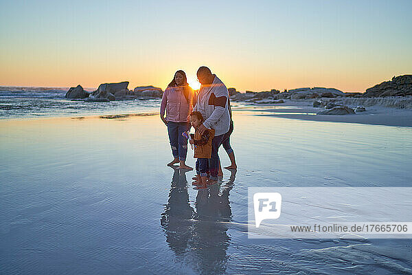 Family wading in wet sand on ocean beach at sunset