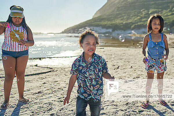 Sisters and brother with Down Syndrome playing with bubbles on beach