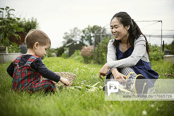 Happy mother watching son with vegetables in garden grass