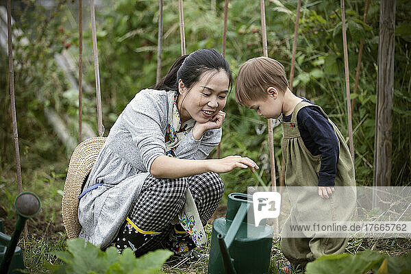 Mother and toddler son with watering can in garden