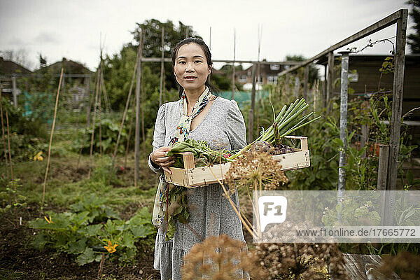 Portrait confident woman with crate of harvested vegetables in garden