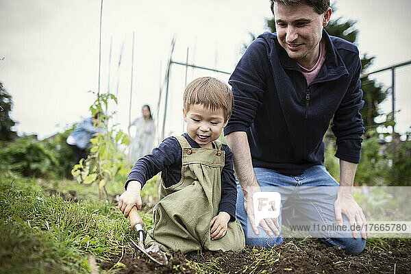 Father and son digging in garden dirt with trowel