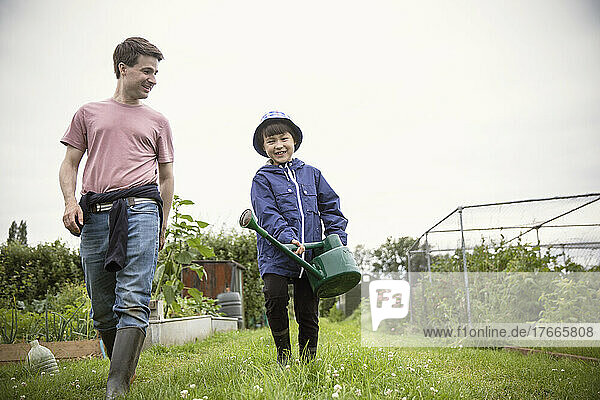 Father and son with watering can walking in garden