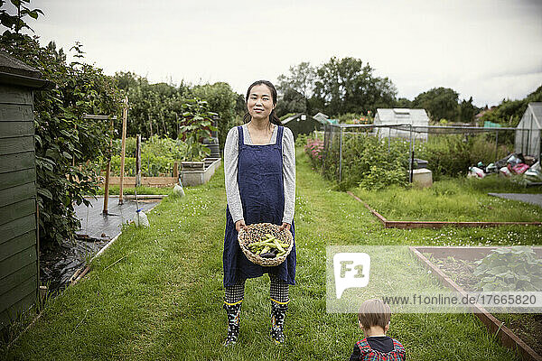 Portrait smiling woman with basket of vegetables in garden