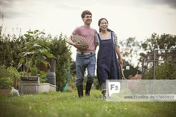 Happy couple walking with vegetables and pitchfork in garden
