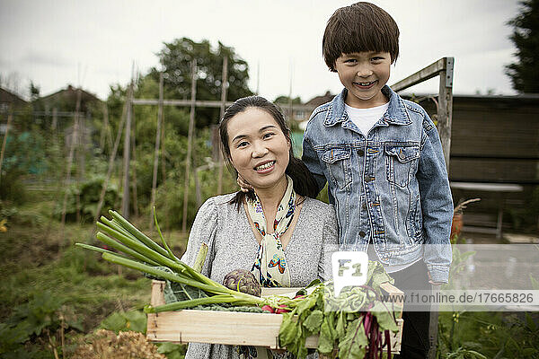 Portrait happy mother and son with harvested vegetables in garden
