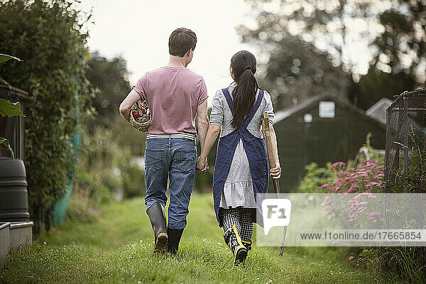 Couple walking with pitchfork and vegetables in garden