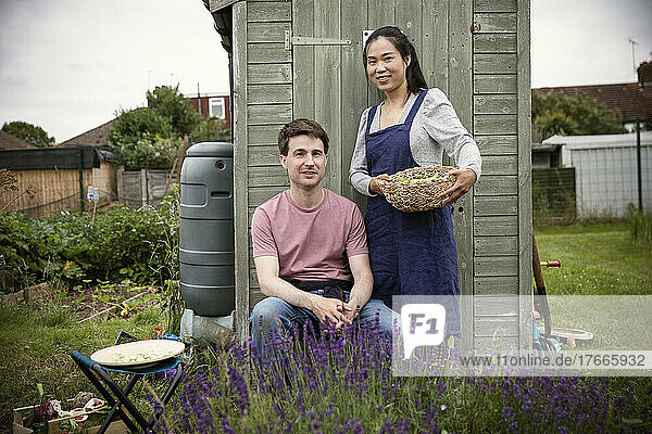 Portrait smiling couple with basket of vegetables in garden