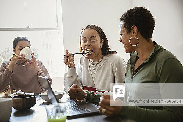 Mother and young adult daughters eating at laptop