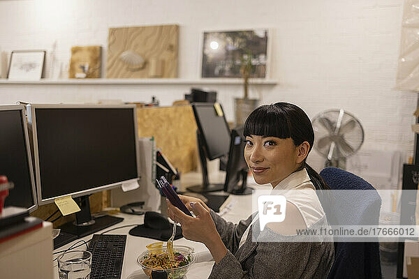 Portrait confident businesswoman eating lunch at office desk