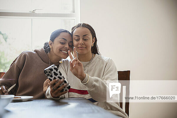 Smiling  cool young adult sisters taking selfie with smart phone