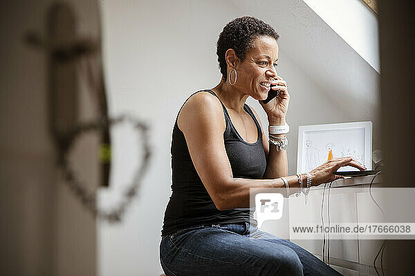 Mature woman talking on smart phone in home office