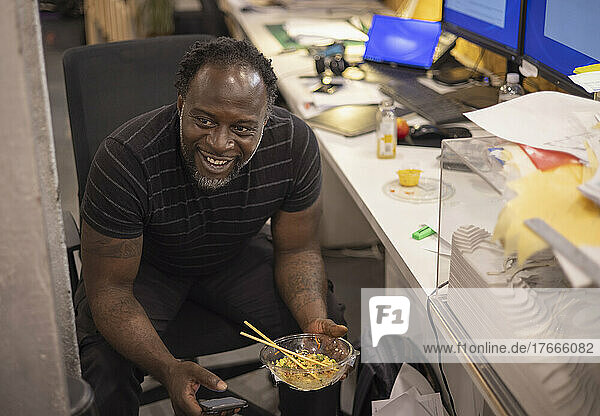 Smiling businessman eating takeout lunch at desk