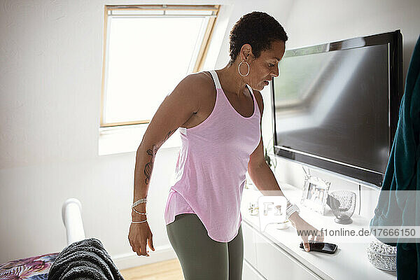 Athletic woman reaching for smart phone in bedroom
