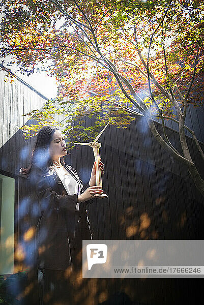 Woman holding wind turbine model in sunny courtyard