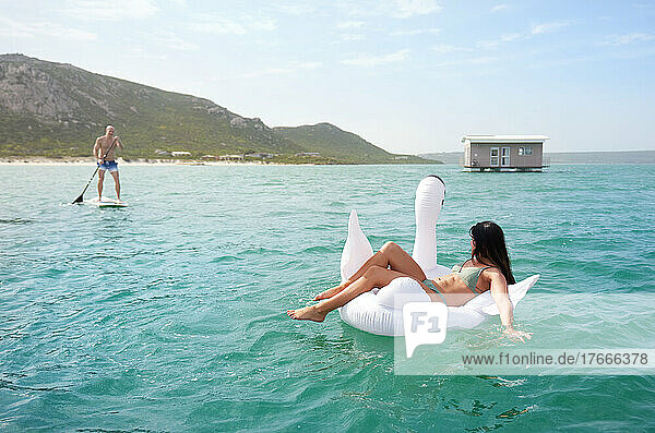Couple on inflatable swan and paddle board on summer ocean