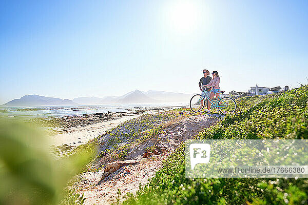 Couple with bicycle on sunny  sandy ocean beach path