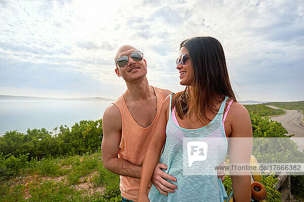 Happy couple in sunglasses and tank tops on ocean beach