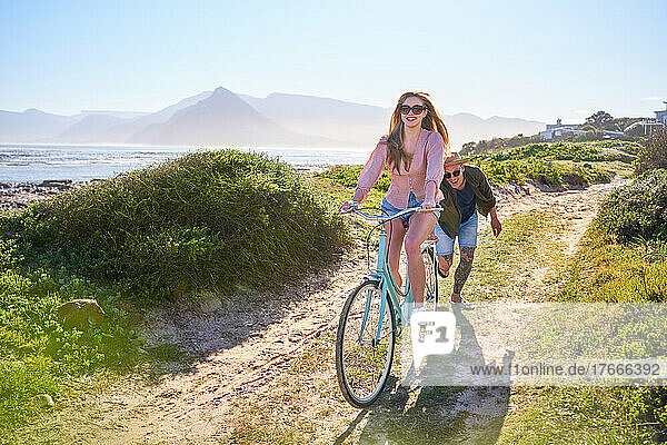 Carefree couple riding bicycle on sunny summer beach path