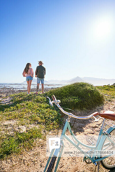 Couple enjoying sunny summer ocean view from beach behind bicycle