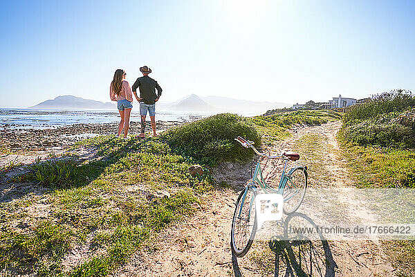 Couple standing on sunny sandy summer ocean beach with bicycle
