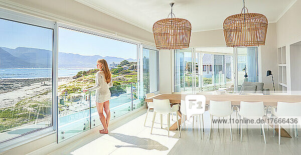 Young woman standing at sunny  luxury patio door with ocean view