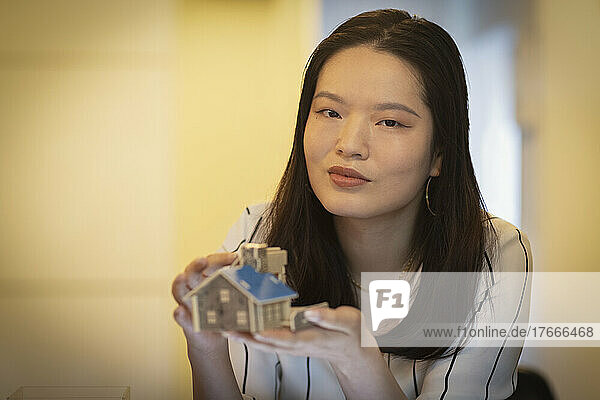 Portrait confident female architect holding tiny house model