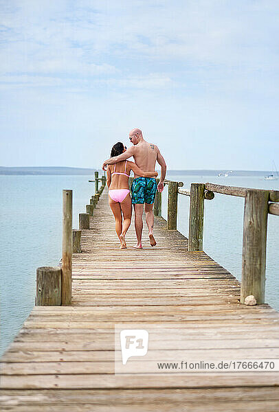 Affectionate couple hugging and walking on wooden pier