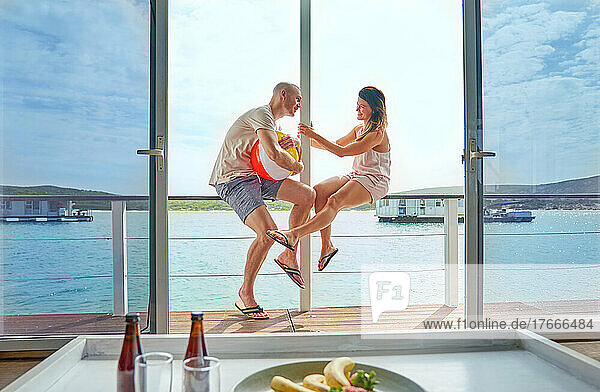 Happy couple with beach ball on sunny houseboat patio