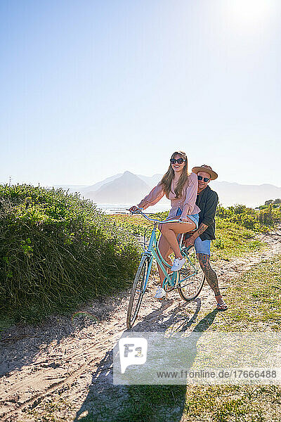Happy couple riding bicycle on sandy summer beach path